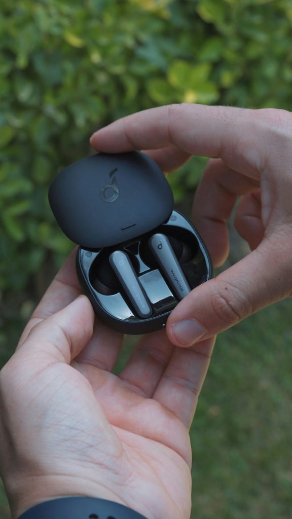 Holding black wireless earbuds with charging case